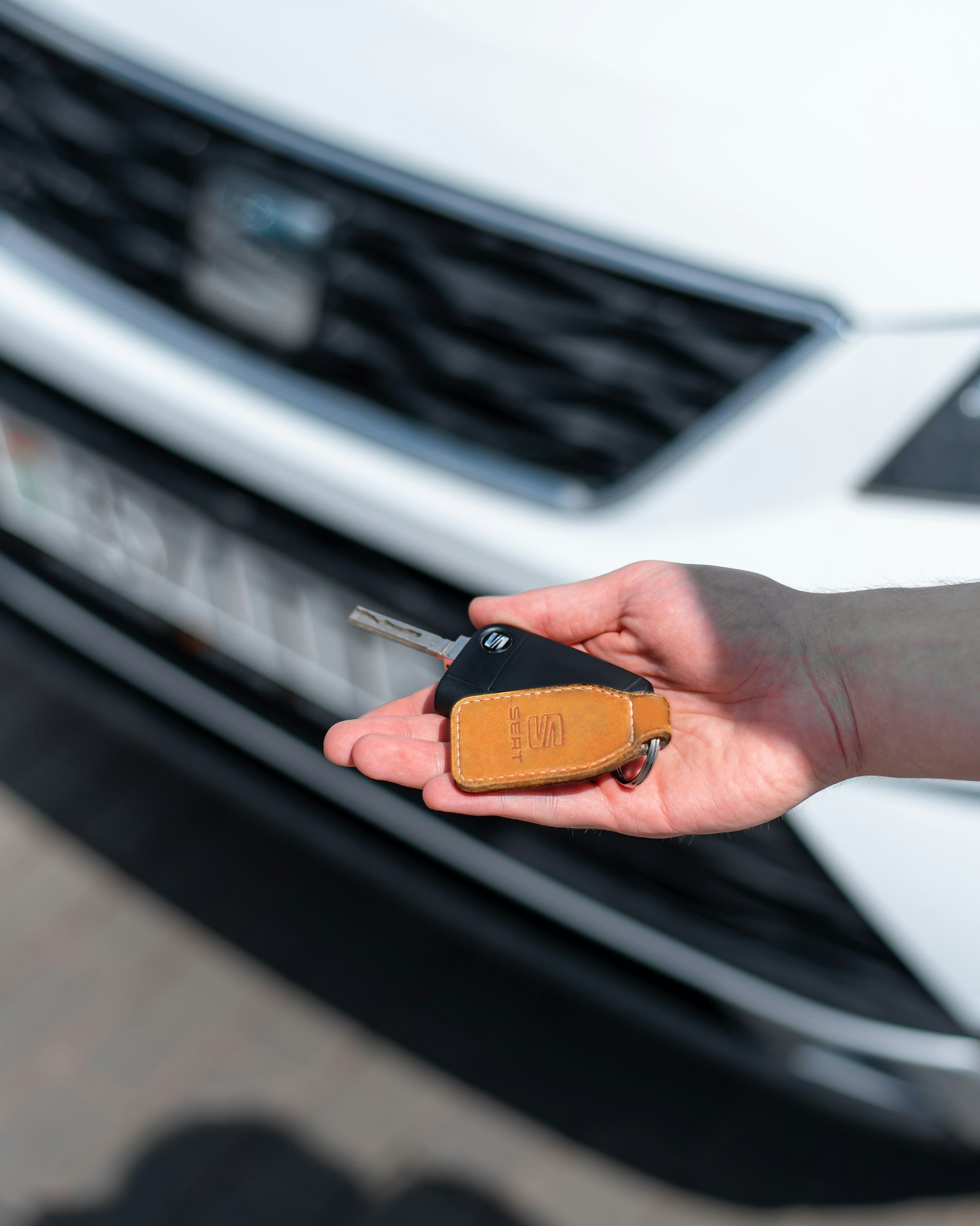 A person holding a car key in an open palm in front of a white car