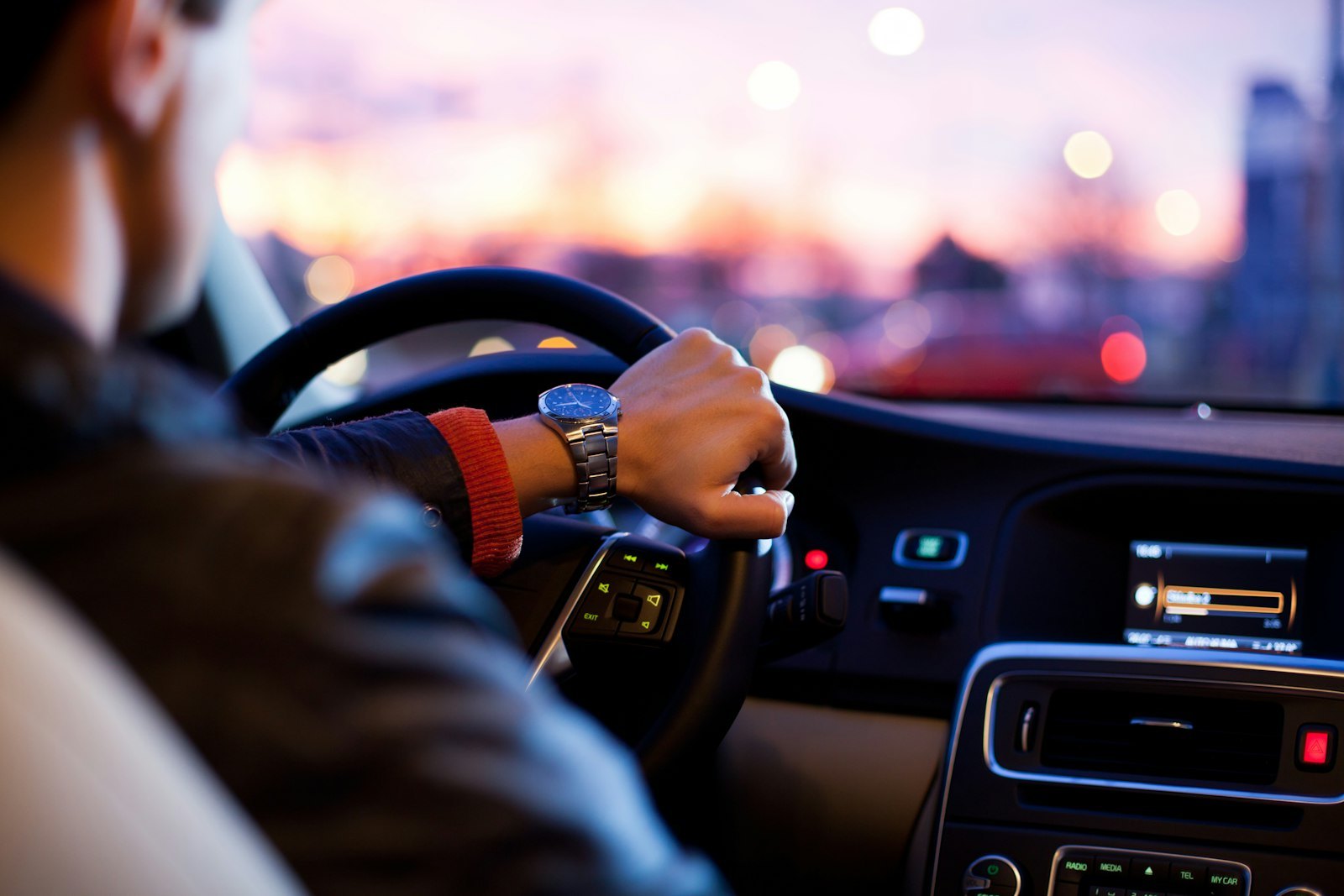 A driver with a wristwatch holding the steering wheel of a car at dusk